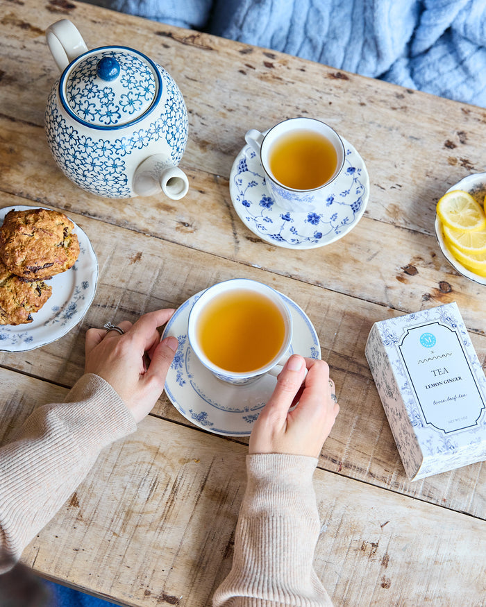 Tea time setting with a teapot, cups, cookies, and lemon slices on a wooden table, featuring Lemon Ginger from the Martha Stewart x Maman collection.